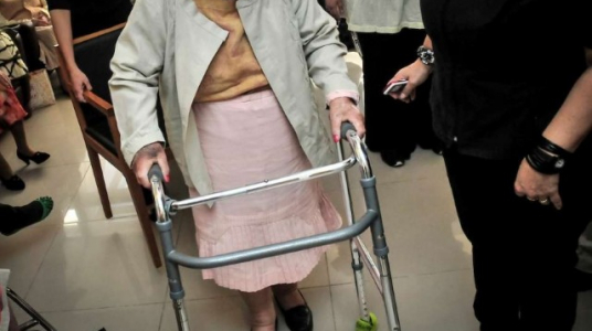 Imagen de una persona mayor con andador acompañada.