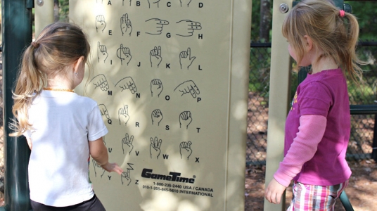 Fotografía de dos niñas mirando un panel con señas y su significado en el lenguaje de señas