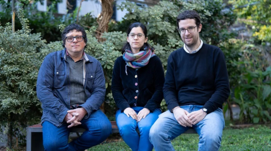 Nicolás Rodriguez junto a dos personas más, sentados en un banco del patio de facultad de psicología