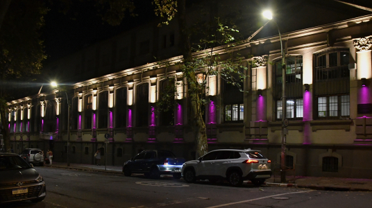 Vista nocturna de la fachada del edificio central de la Facultad de Psicología, iluminada en color violeta.