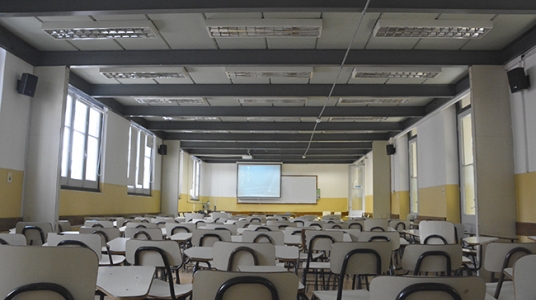 Fotografía desde el fondo del salón 1 en la que se ven silla, los parlantes colocados, y el pizarrón al fondo