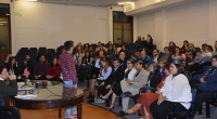 Fotografía durante la actividad. Se aprecia el auditorio con egresados/as y sus familiares y el Docente Bruno Cancio de espaldas tomando la palabra.