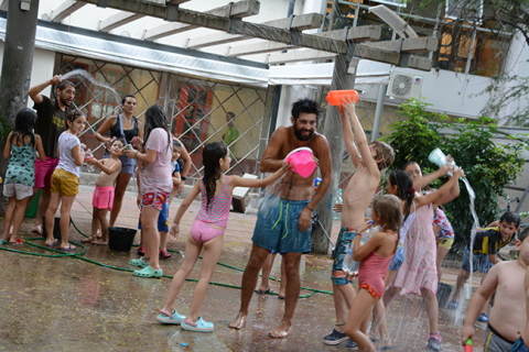 Fotografía de niños y sus recreadores jugando a la "guerra de agua" en el patio de la Facultad